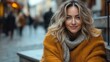 © Denis - A woman with wavy hair wearing an orange sweater and a gray scarf smiles warmly while sitting on a stone step in a bustling street during a cool autumn afternoon