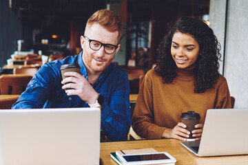 Happy smiling multicultural male and female freelancers enjoying coffee break for watching funny videos online on web page using 4g connection on laptop device during leisure time togetherness