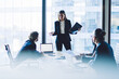 © BullRun - Puzzled female director in elegant suit communicating with employees during working process in conference room standing near meeting table with modern technology, laptop with mock up for website