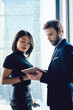 © BullRun - Male and female lawyers checking information on touch pad standing near skyscraper window in office, successful diverse employees reading financial news on digital tablet, colleagues collaborating