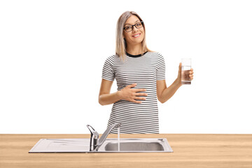 Sticker - Young woman holding a glass of water behind a kitchen sink