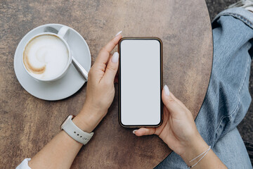 Mockup woman's hand holding using smart phone with white blank screen POV at coffee shop, mobile app design and advertising, online marketing