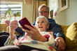 © Marko Geber - Happy senior couple on couch using smartphones together at home