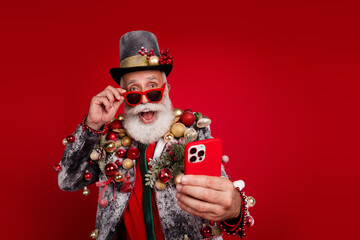 Sticker - Photo of happy cheerful old man excited hold device wear christmas tree balls costume sunglasses isolated red color background