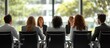 © MBRAMO - Rear view of businesspeople sitting at a table in a conference room during a meeting.