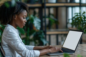 Close-up shot of an African American businesswoman working on a laptop with a blank screen on her desk in a modern office setting.