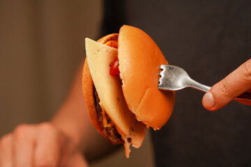 Ready to eat tasty fast food hamburger. Unhealthy food concept. Hands holding homemade beef burger on wooden table. Man holds burger with hands. Home delivery. Close up shot of young man eats burger.