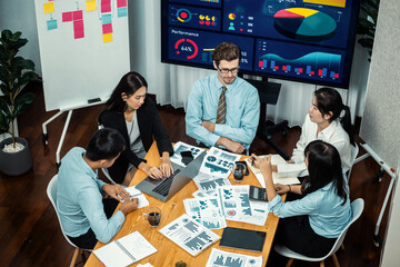 Wide top view of diverse group of business analyst team analyzing financial data report paper on meeting table. Chart and graph dashboard by business intelligence analysis. Meticulous