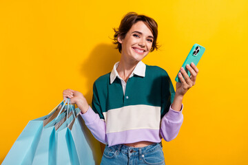 Sticker - Photo of positive cute lady dressed polo shirt rising shoppers chatting modern device isolated yellow color background