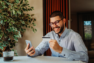 Young caucasian man shopping online on mobile phone using credit card	