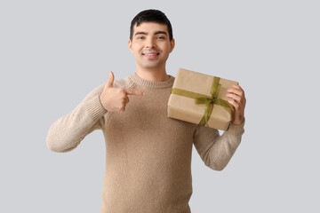 Wall Mural - Happy young man with gift showing thumb-up on light background