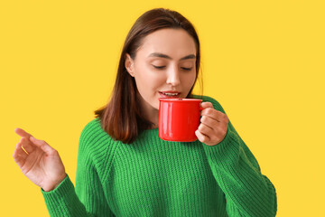 Poster - Beautiful young woman with cup of hot mulled wine on yellow background