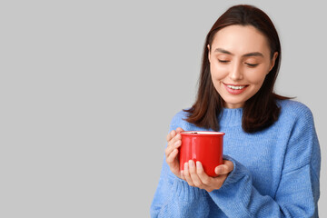 Wall Mural - Beautiful young woman with cup of hot mulled wine on grey background