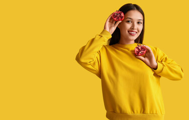 Poster - Beautiful young Asian woman with fresh pomegranate on yellow background