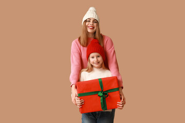 Poster - Cute little girl and her mother with Christmas gift box on brown background