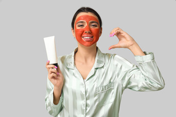 Poster - Beautiful young woman with facial mask making half of heart on grey background