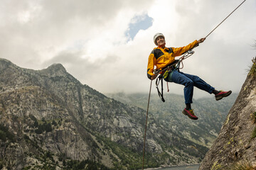 A woman is hanging from a rope on a mountain. She is wearing a yellow jacket and blue pants