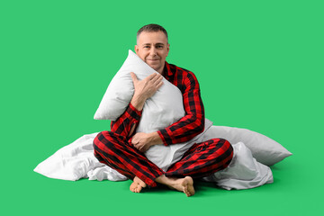 Poster - Handsome mature happy man in checkered pajamas with pillow and blanket on green background