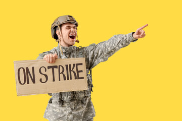 Wall Mural - Protesting male soldier holding placard with text ON STRIKE and pointing at something against yellow background