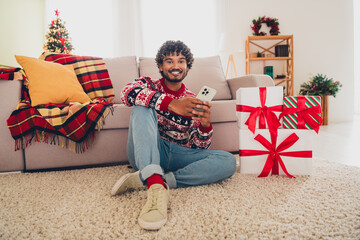 Poster - Full body portrait of nice young man sit carpet floor hold phone giftbox wear x-mas sweater holiday atmosphere flat indoors