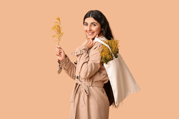 Wall Mural - Happy young woman holding eco bag with mimosa flowers on beige background