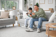 © Pixel-Shot - Cute little boy with his father playing video game on sofa at home