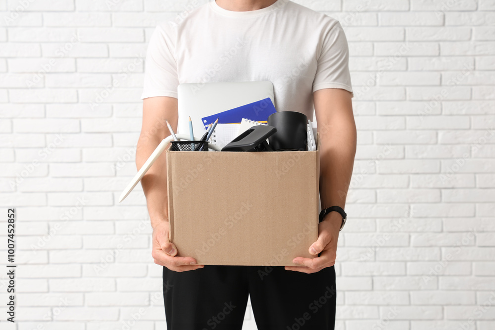 Fired young man holding box with personal stuff on white brick background, closeup