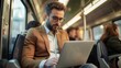 © Vilaphon  - Businessman using his commute time to work on a laptop, sitting in a train seat with other commuters around