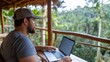 © LifeMedia - A person is in a rustic treehouse, working on their laptop with a serene view of the lush green forest, embodying tranquility and modern simplicity.