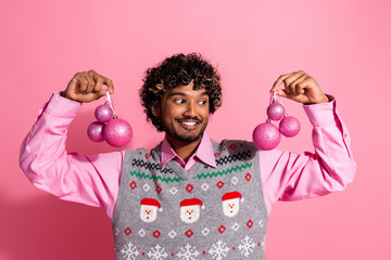 Wall Mural - Portrait of nice young man hold glossy tree ball toys wear xmas new year vest isolated on pink color background