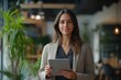 © Goat_Team - Confident Woman in Modern Office Holding Tablet