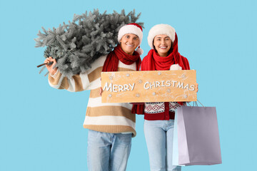 Canvas Print - Young couple with Christmas tree, shopping bags and MERRY CHRISTMAS sign on blue background