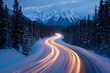 © Mikki Orso - Long exposure of car lights on snowy mountain road at dusk with forest and blue hour glow