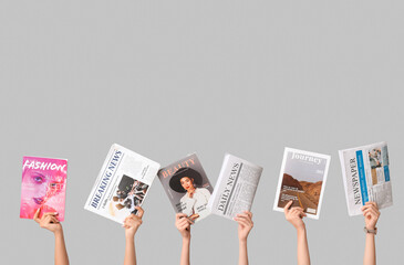 female hands with different magazines and newspapers on grey background