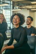 © THEPRZ - Happy young African American woman sharing a light-hearted moment with diverse colleagues in a modern office environment, promoting workplace camaraderie and positive team dynamics