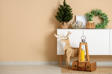 Poster - Christmas lantern with candle on suitcase and wooden deer near chest of drawers with Christmas decorations in room