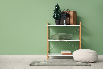 Poster - Shelving unit with  Christmas tree, suitcase, lantern and pouf near green wall