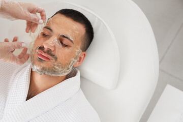 Canvas Print - Beautician applying cosmetic gel mask on handsome man's face in spa salon