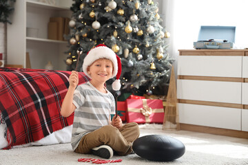 Sticker - Cute little boy in Santa hat playing glucophone at home on Christmas eve