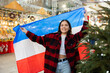 © JackF - Cheerful young girl holding national flag of Netherlands, standing outdoors against blurred background of illuminated shopping stalls at traditional Christmas city market..