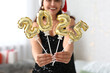 © Pixel-Shot - Beautiful young woman with figure 2025 made of foil balloons in living room. Christmas celebration