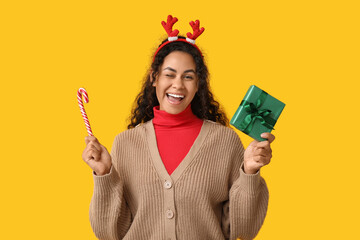 Sticker - Happy African-American woman with Christmas gift and candy cane on yellow background