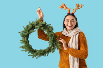 Poster - Young woman in reindeer horns with Christmas wreath on blue background