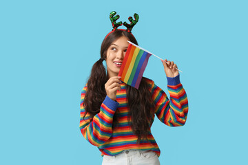 Sticker - Young Asian woman in Christmas reindeer horns with LGBT flag on blue background