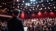 © Luxetify - A speaker in a suit stands in front of a large audience in a hall with red walls and bright lights.