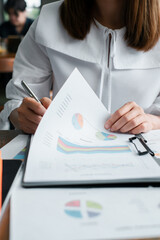 Close-up of a businesswoman reviewing financial documents with charts and graphs, highlighting data analysis and business strategy.