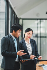 Wall Mural - Two business professionals in formal attire discussing documents in a modern office with large windows.