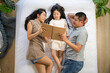 © ultramansk - A family enjoys quality time together, reading a book while lying on the bed. The parents and their daughter share a relaxing moment, strengthening their bond in a peaceful home environment.