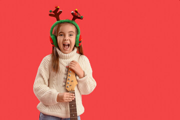 Cute little girl in Christmas reindeer horns with guitar on red background