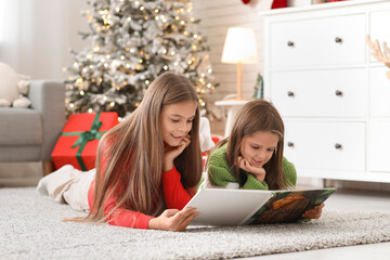 Poster - Cute happy little girls with book reading Christmas story at home